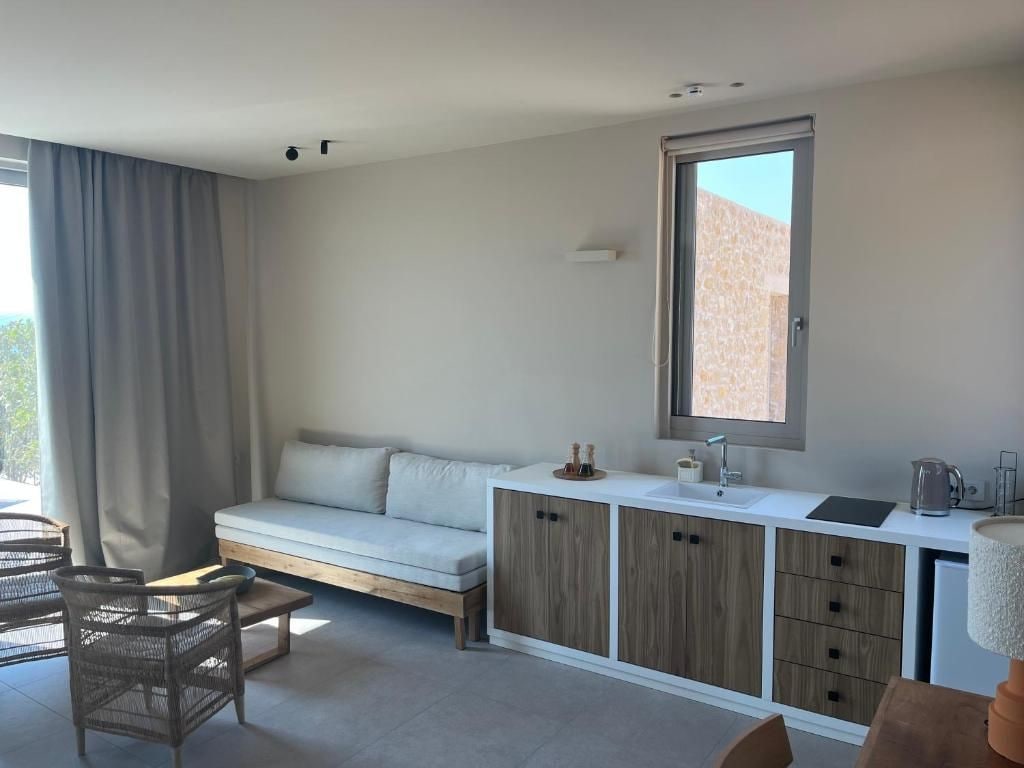 A modern living room with a sofa, a dining table, and a kitchen area with cabinets and a window.