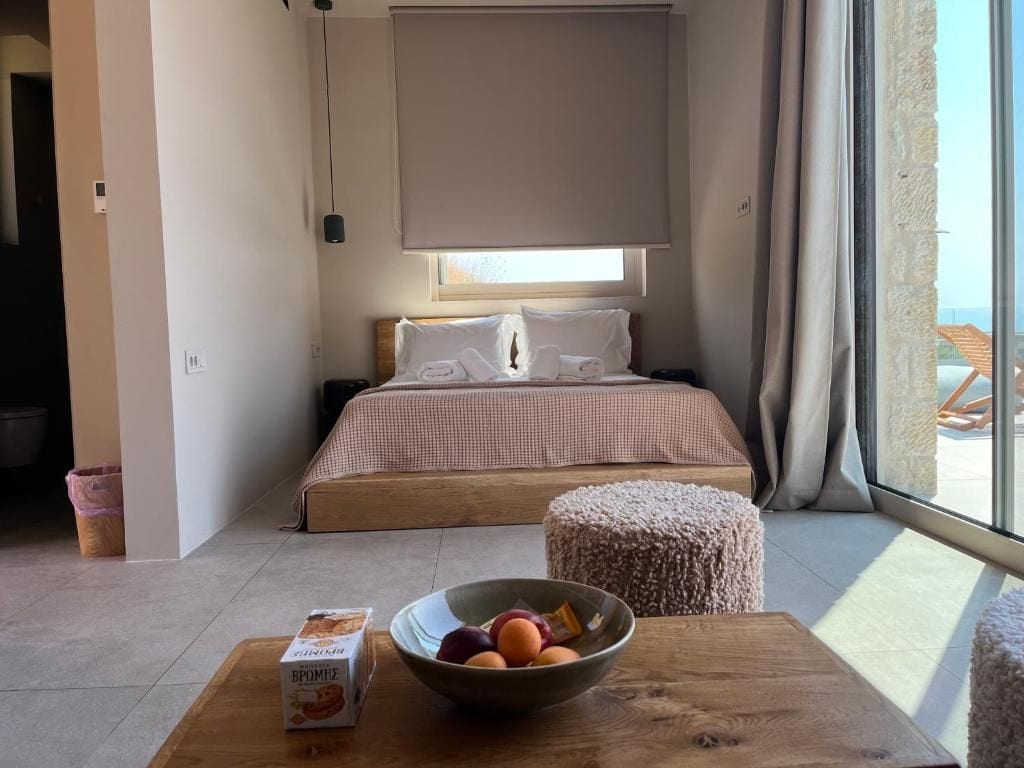 A bedroom with a bed, a bedside table with a bowl of fruit, and a window with curtains.
