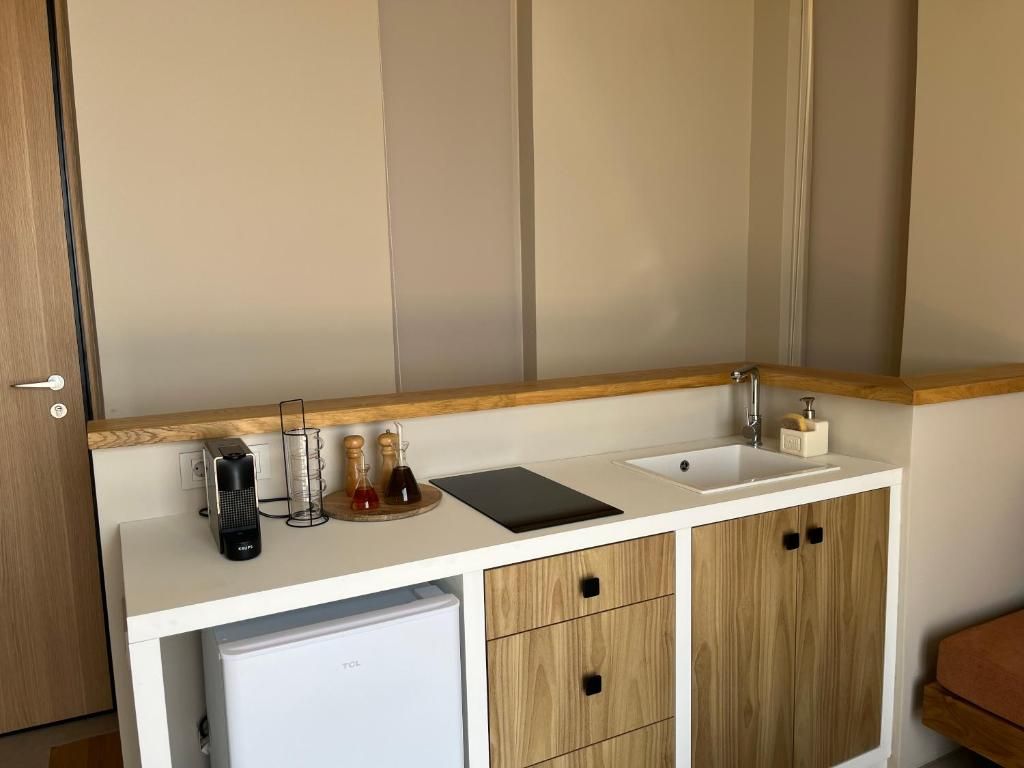 Une petite cuisine équipée d’un plan de travail blanc, d’un évier, d’un petit réfrigérateur et de placards en bois.