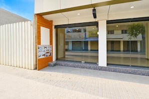 A modern building entrance with a glass facade, a wooden door, and a small outdoor seating area. - Super Townhouse Banaswadi Railway (Bangalore)