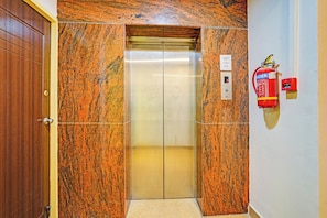 Un ascensor amb paret de marbre, un extintor fixat a la paret i una porta amb pom de bronze.