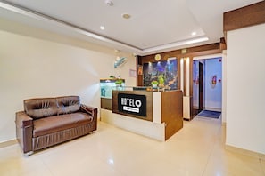 A hotel reception area with a brown leather sofa, a reception desk with a 'HOTEL' sign, and a cityscape mural on the wall. - Super Townhouse Banaswadi Railway (Bangalore)