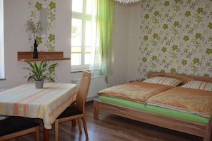 A room with a bed, a table, and a chair. There is a window with curtains. - Holiday apartment with 1 bedroom (Neustrelitz)