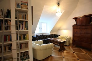 A room with a sloped ceiling, a bookshelf, a sofa, a table, and a wooden cabinet.