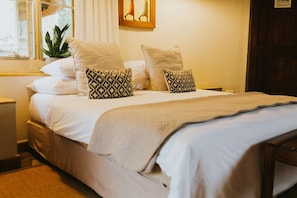 A neatly made bed with white bedding and patterned pillows, a bedside plant, and a framed picture on the wall. - Mohlabetsi Safari Lodge (Hoedspruit)