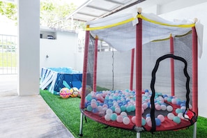 Un trampolino con rete di sicurezza, circondato da palline colorate, sotto una zona coperta con erba sintetica.