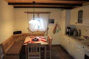 A dining area with a wooden table and benches, a hanging light fixture, and a kitchen with white cabinets and appliances. - Holiday home in spa town Jonsdorf with sauna (Kurort Jonsdorf)