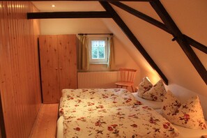 A bedroom with a sloped ceiling, wooden wardrobe, a bed with floral bedding, and a window with curtains. - Holiday home in spa town Jonsdorf with sauna (Kurort Jonsdorf)