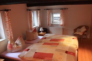 Een slaapkamer met een bed, kussens, een stoel, een raam met gordijnen en een radiator.