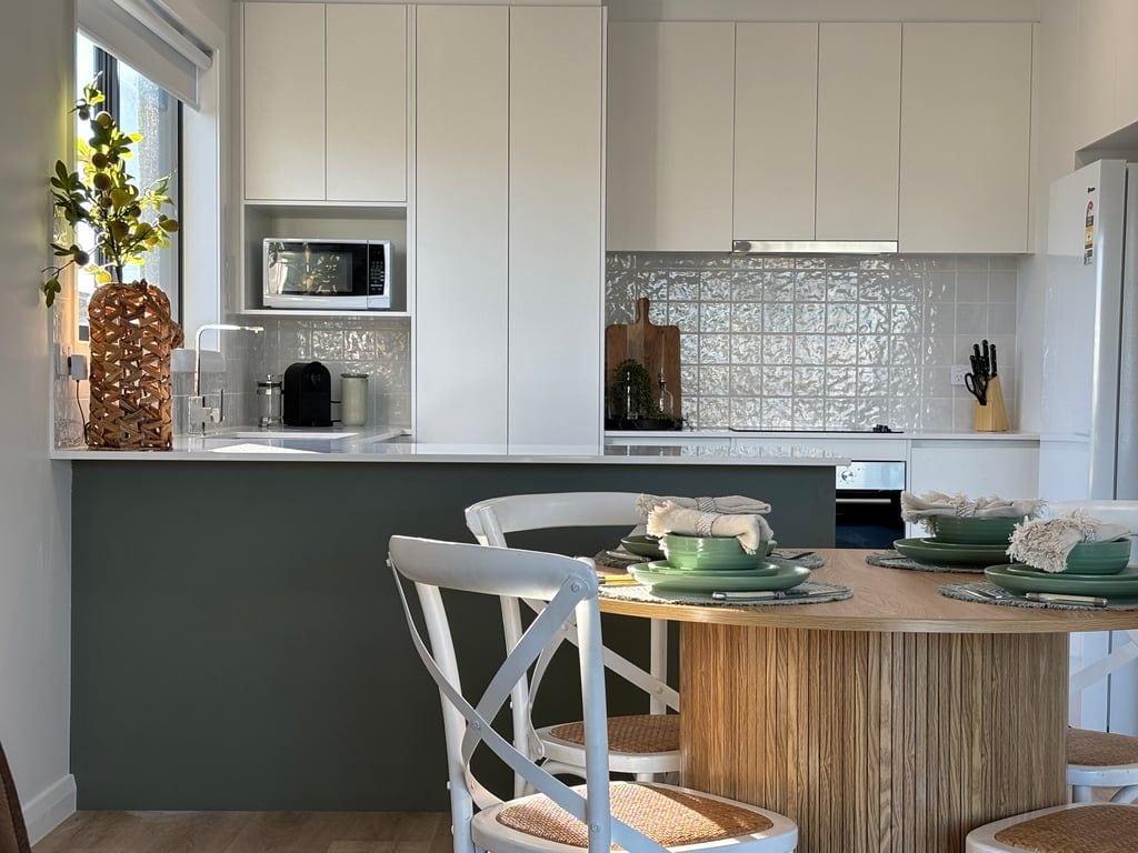 A modern kitchen with white cabinets, a microwave, and a dining area with a wooden table and chairs.