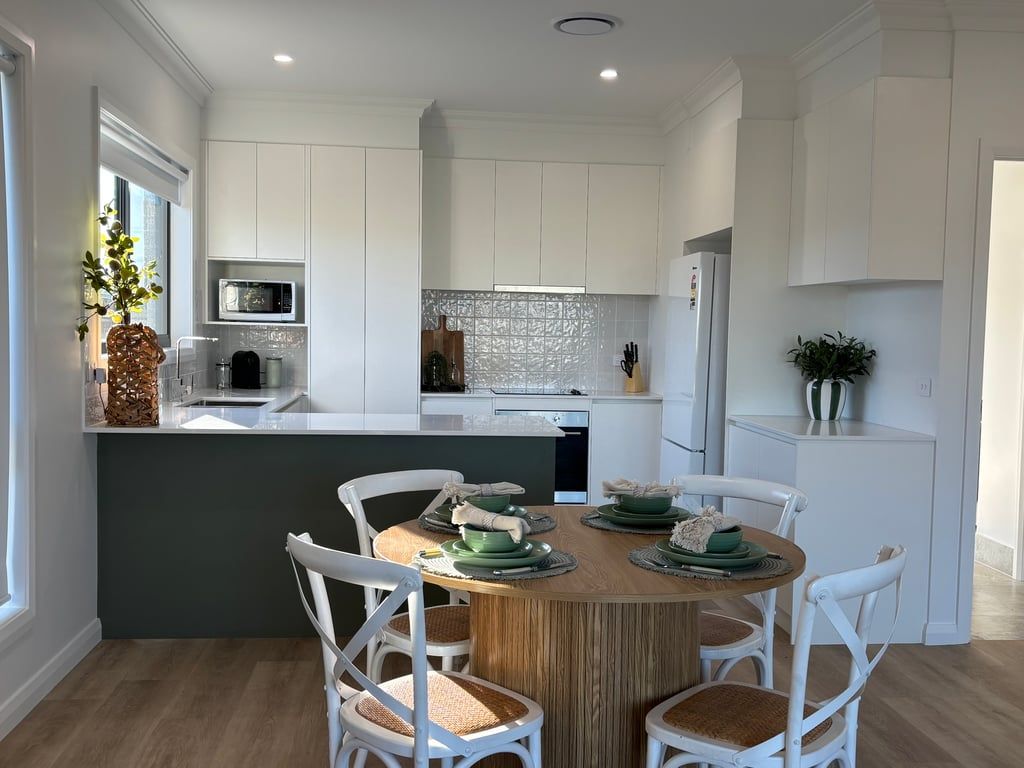 A modern kitchen with white cabinetry, a central island with seating, and a dining area with white chairs.