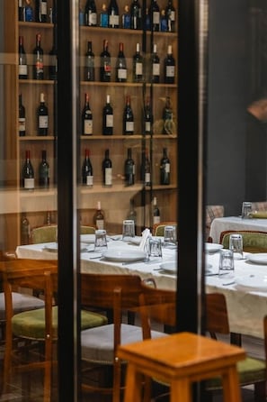 A restaurant interior with multiple tables, chairs, and a wine rack with various bottles. - Oxygen Boutique Hotel Tirana (Tirana)