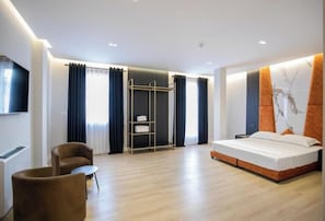 A modern hotel room with a bed, a seating area with a chair and a small table, a wardrobe, and a television mounted on the wall. - Oxygen Boutique Hotel Tirana (Tirana)