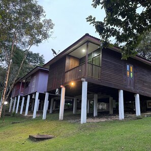 A two-story wooden house with a balcony, supported by white pillars, surrounded by trees. - Lilla Hilltop Retreats (Janda Baik)