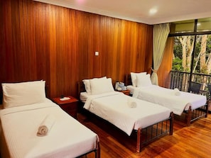Une chambre d’hôtel avec trois lits simples, des lambris en bois sur les murs et un balcon avec vue sur les arbres.