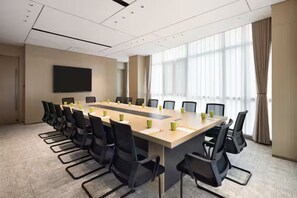 Un salón de conferencias con una mesa larga, sillas, un televisor de pantalla plana y ventanas grandes.