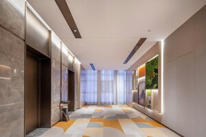 Un pasillo moderno de hotel con paredes de mármol, alfombra estampada y un panel verde decorativo.