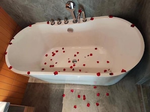 A bathtub with rose petals scattered around it. - Home2 Suites by Hilton Liaocheng Dongchang (Liaocheng)