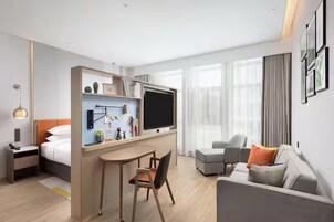 Una habitación de hotel moderna con una cama, un escritorio con televisor de pantalla plana, un sofá y un comedor.