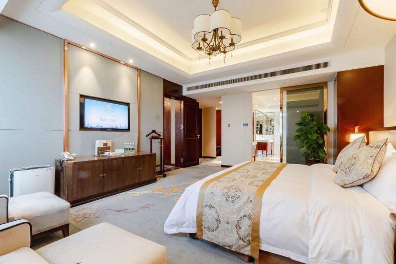 A hotel room with a large bed, a desk, a television, and a plant.