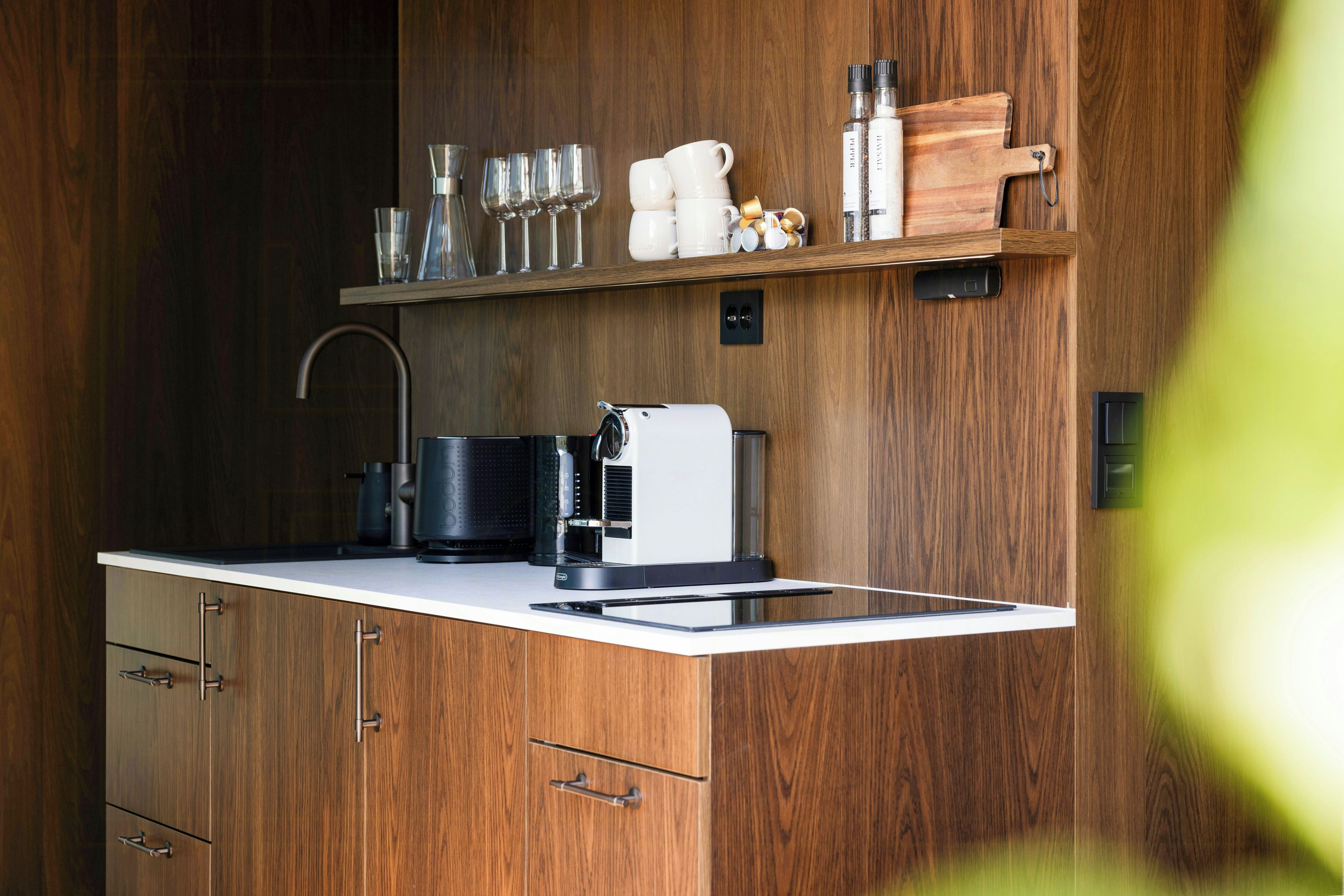 Cozinha moderna com armários de madeira, máquina de café integrada e bancada com diversos utensílios de cozinha.