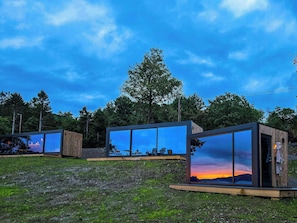 Una estructura moderna al aire libre con paredes de vidrio, terraza de madera y zona de estar.
