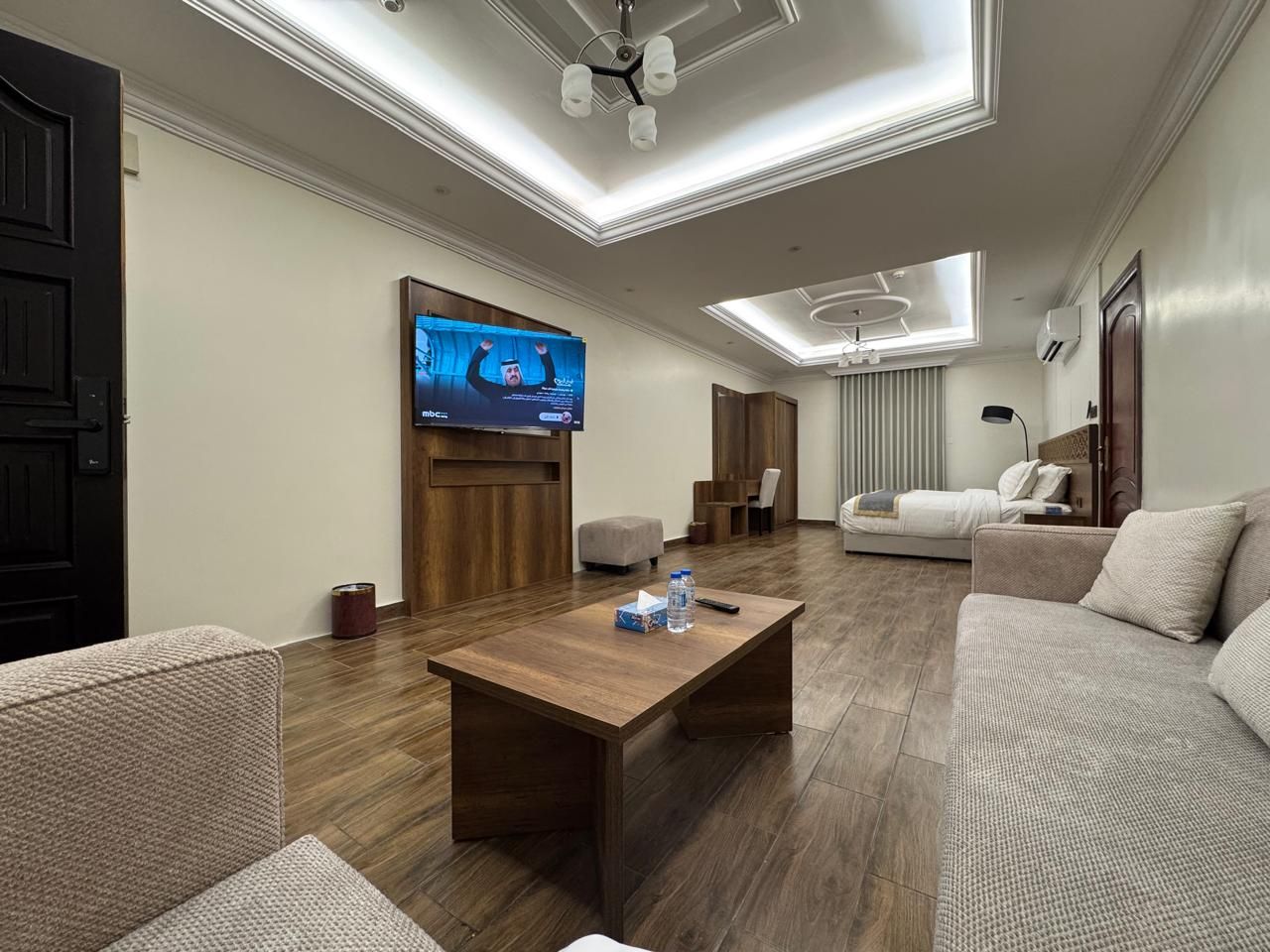 Una sala de estar moderna con una mesa de centro de madera, sofás, un televisor de pantalla plana y una lámpara de techo.