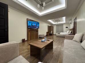 A modern living room with a wooden coffee table, sofas, a flat-screen TV, and a ceiling light fixture. - Majed Studio (Jeddah)