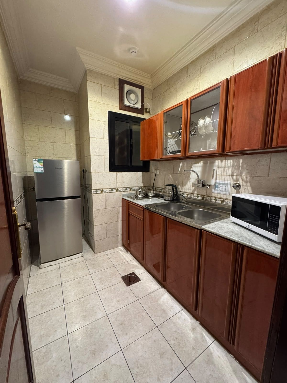 Una cocina con un refrigerador de acero inoxidable, un microondas y gabinetes de madera.