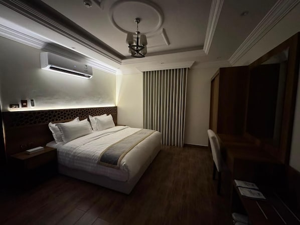 A hotel room with a bed, bedside table, nightstand, wall-mounted air conditioner, and a ceiling light fixture. - Majed Studio (Jeddah)