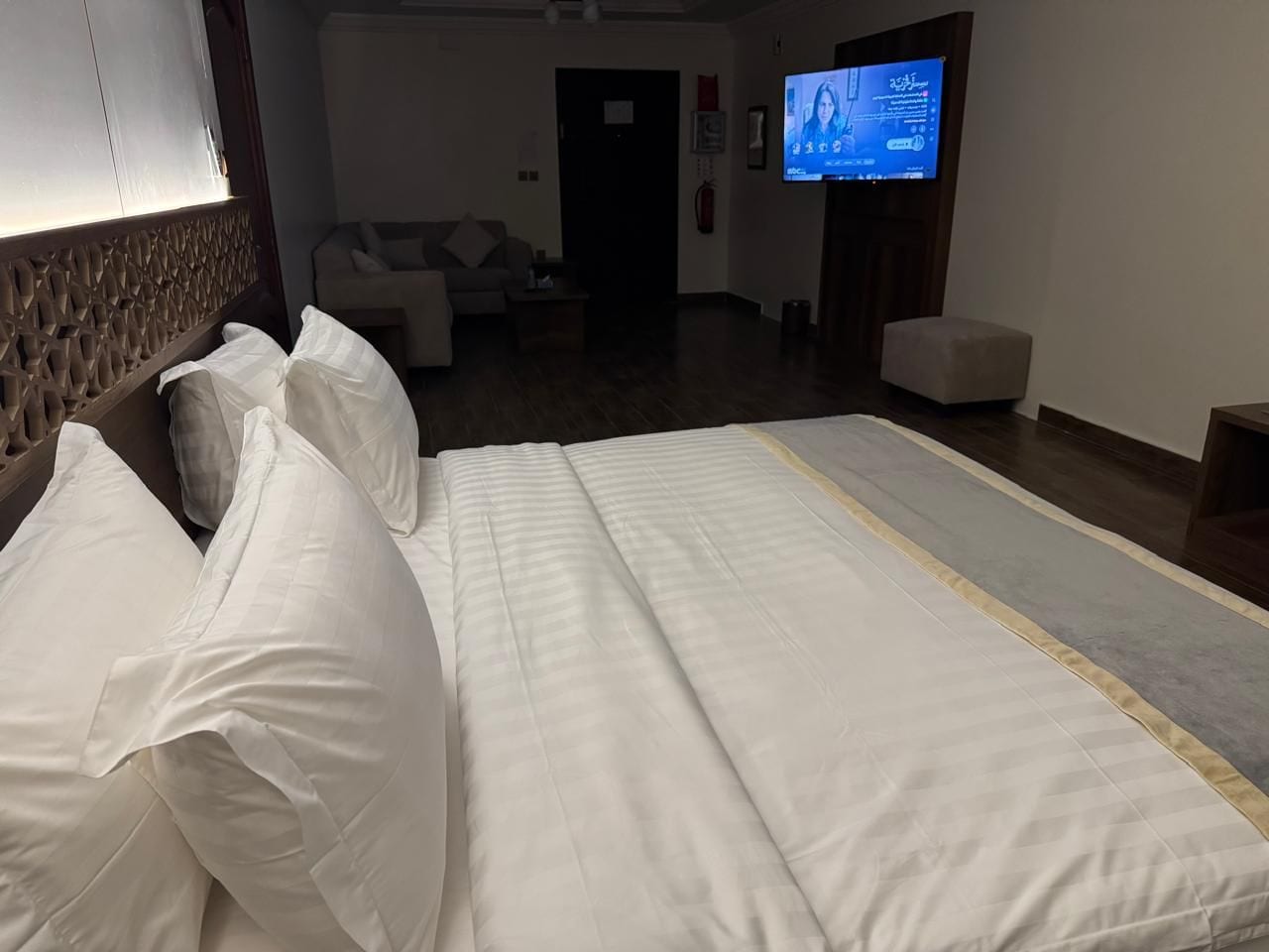 A hotel room with a bed, a television, a sofa, and a wooden floor.