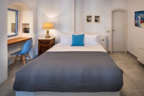 A hotel room with a bed, a desk, a chair, a lamp, and a door. - My Rental Homes - Guest House Skiron, with private pool and sea view (Fira)