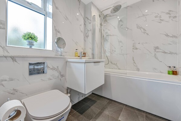 Et badeværelse med toilet, vask, spejl, brusebad og et vindue med en plante.