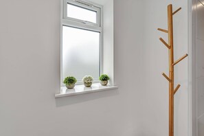 Una ventana con marco blanco, un perchero de madera a la derecha y tres macetas con plantas en el alféizar.