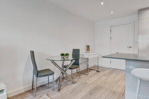 Et moderne køkken med spiseplads, med et bord med glasplade, to stole og en lille potteplante.