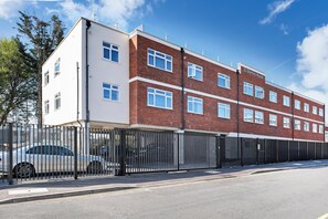 En bygning med flere etager, facade i hvid og rød mursten, lukket parkeringsområde og en klar blå himmel.