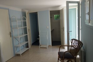 A room with a white metal shelf unit, a wicker chair, and an open door leading to a bathroom. - Vrbo Property (Roquebrune-sur-Argens)