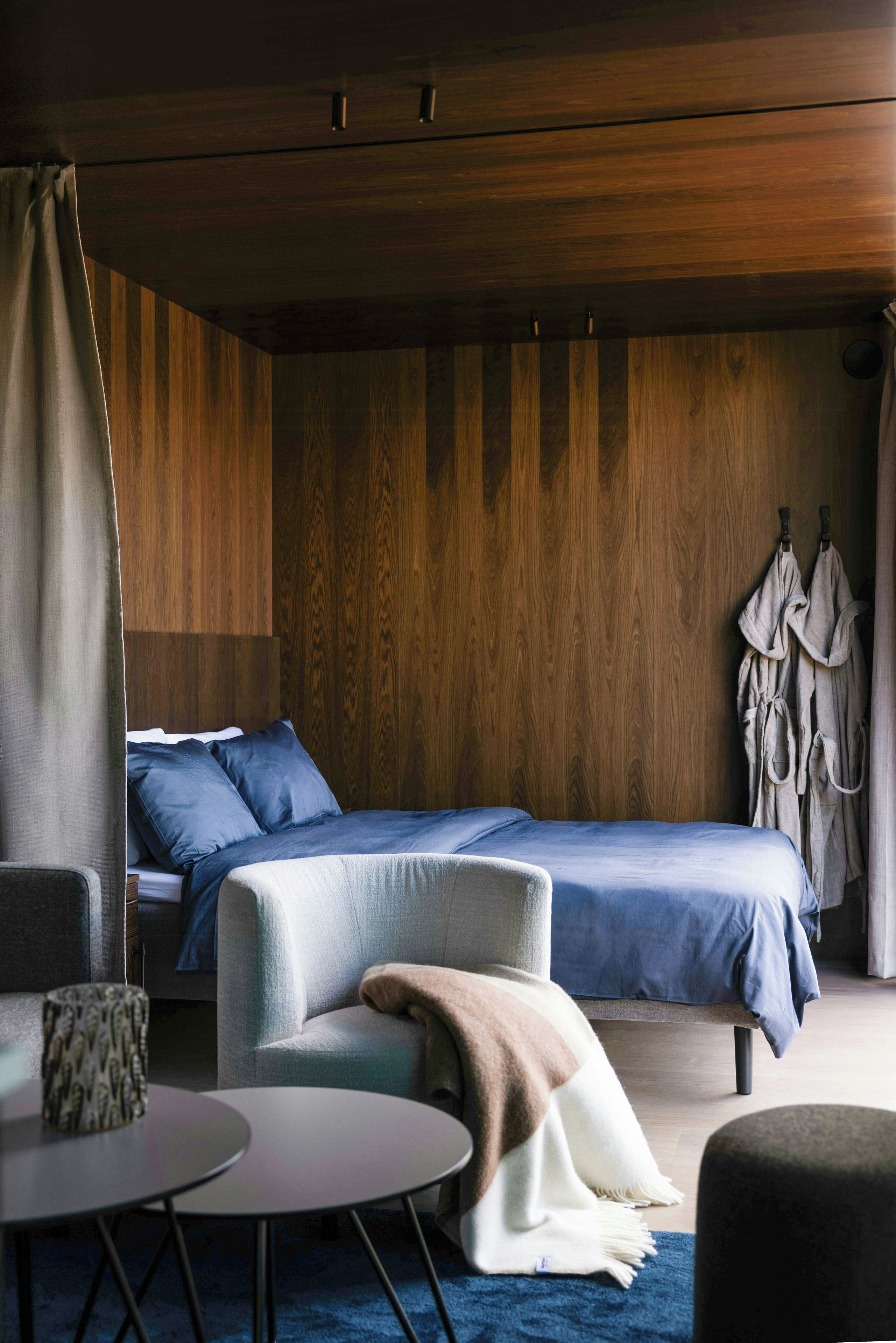 A modern bedroom with a bed, a chair, a table, and a coat rack.