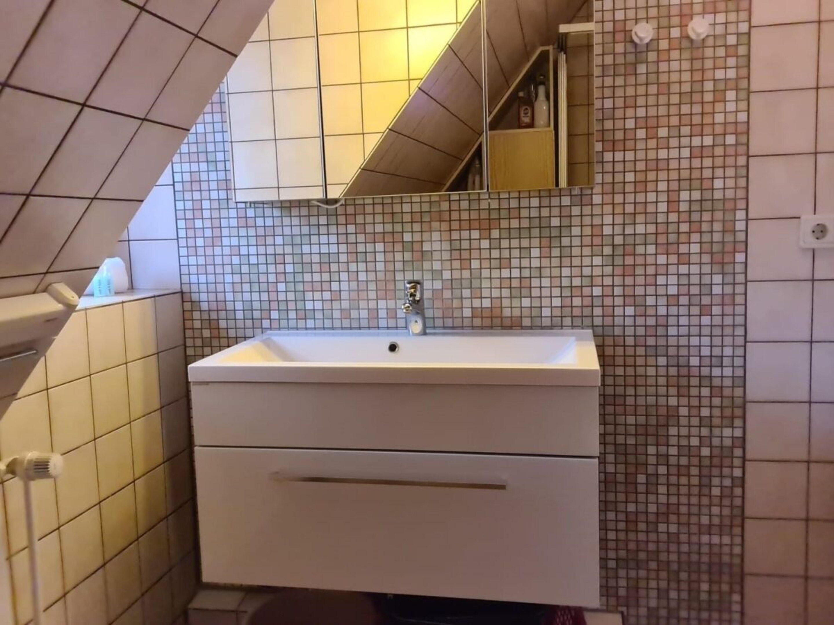 A bathroom with a white sink, a mirror, and tiled walls.