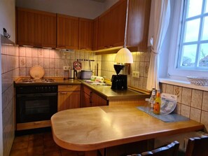 A kitchen with wooden cabinets, a stove, a coffee maker, and a window with a view. - Holiday Home in Nieblum With Swimming Pool (Nieblum)