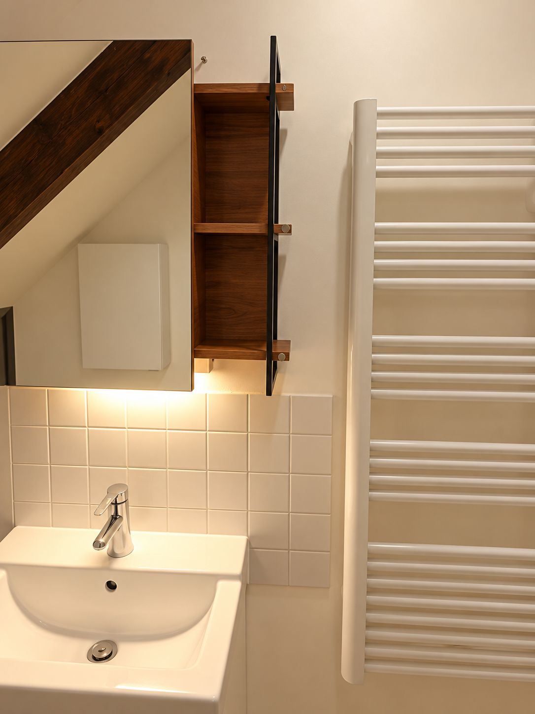Un baño con un lavamanos blanco, un estante de madera y un perchero para toallas.