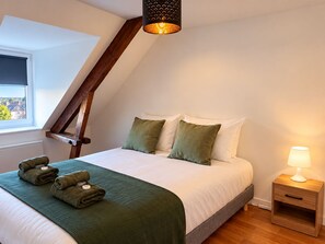 A bedroom with a sloped ceiling, a bed with white and green bedding, a bedside lamp, and a window with a view.