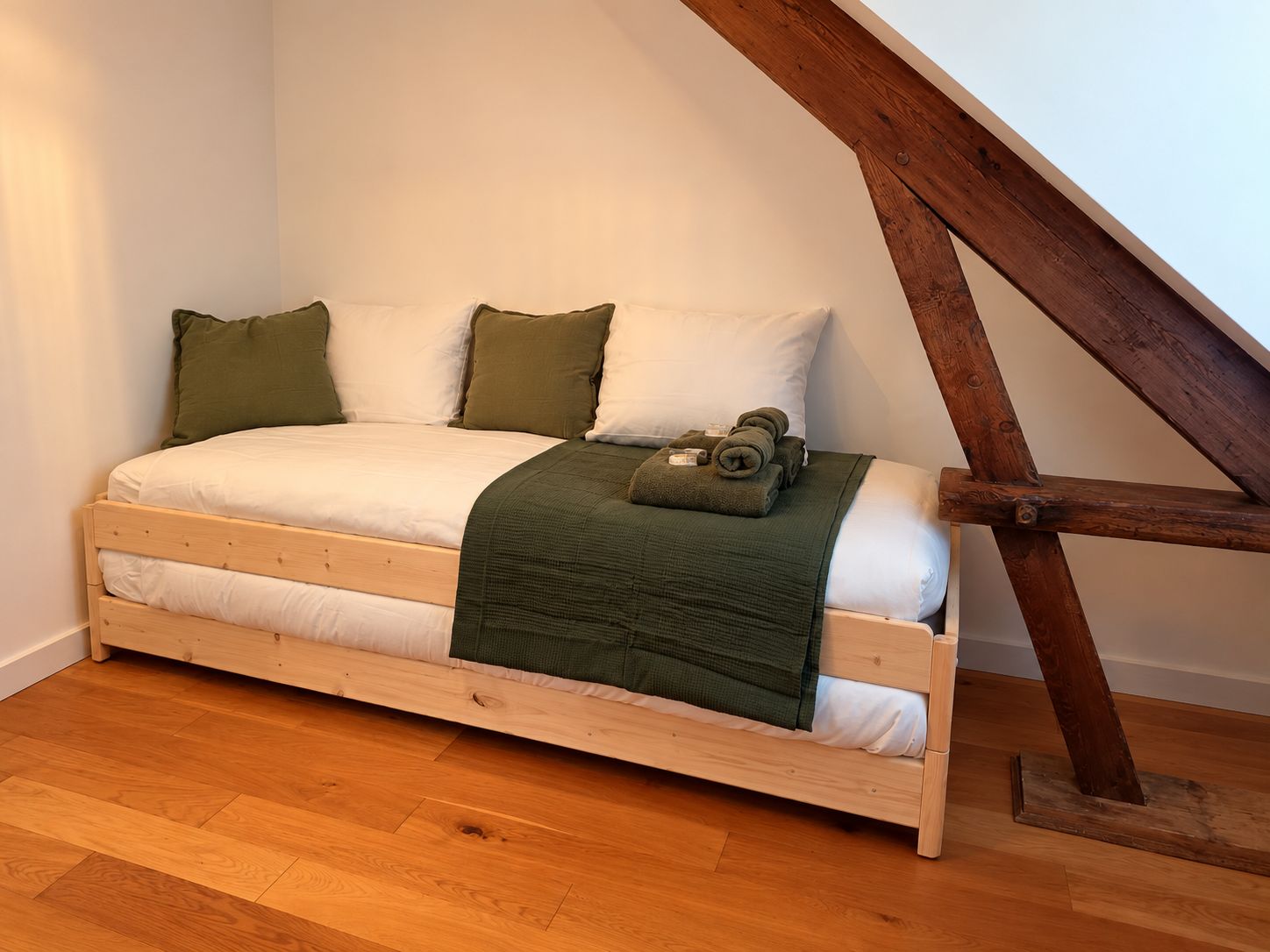 Een eenpersoonsbed met houten frame, wit beddengoed en een groene plaid.