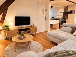Een moderne woonkamer met een flatscreen televisie, houten meubels, een ronde salontafel en een grijze bank.