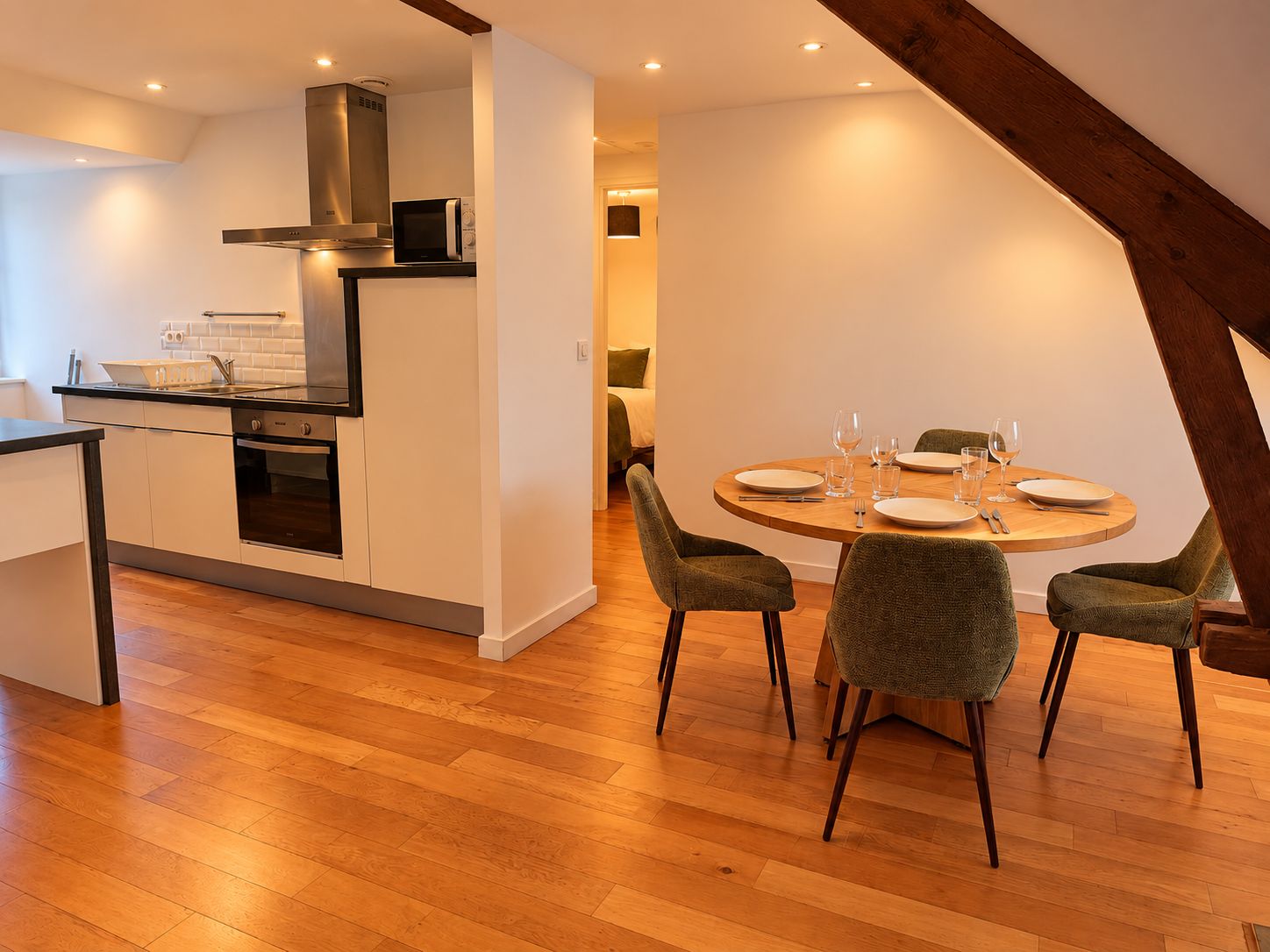 Een moderne keuken met een ingebouwde oven en magnetron, een eethoek met een ronde tafel en vier stoelen, en een zichtbare trap naar een hoger gelegen verdieping.