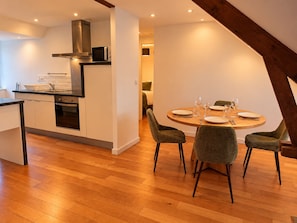 Een moderne keuken met een ingebouwde oven en magnetron, een eethoek met een ronde tafel en vier stoelen, en een zichtbare trap naar een hoger gelegen verdieping.