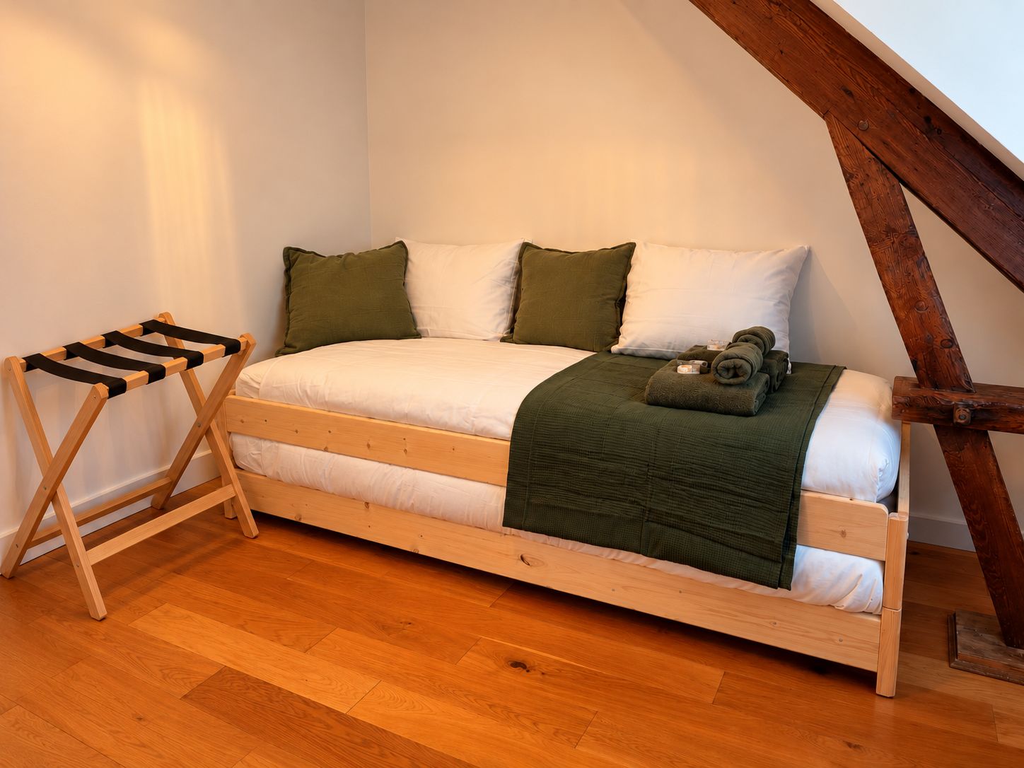 Un lit simple avec un cadre en bois, une couverture verte et une serviette enroulée posée sur le côté.