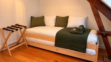 Un lit simple avec un cadre en bois, une couverture verte et une serviette enroulée posée sur le côté.
