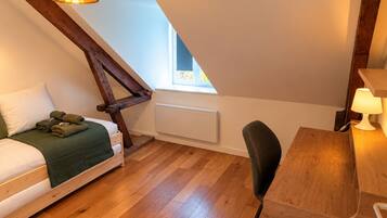 A bedroom with a sloped ceiling, a bed with a green blanket, a wooden desk, and a chair.