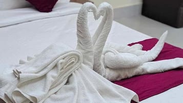 A neatly made bed with a heart-shaped towel arrangement on a white bedspread and a magenta throw.